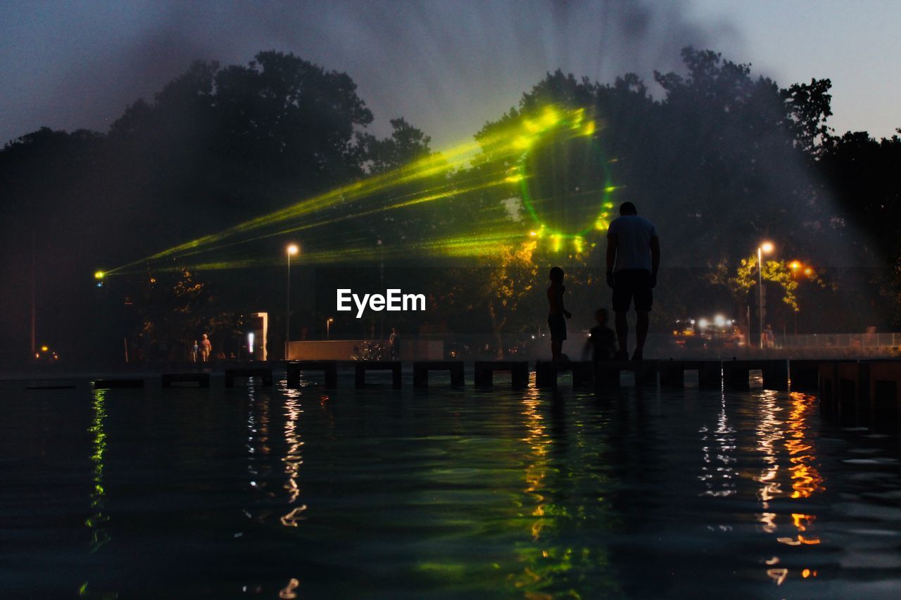 People on pier over lake at night