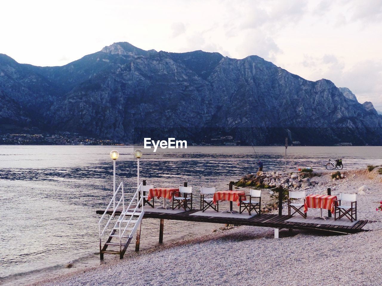 CHAIRS AND TABLE BY SEA AGAINST MOUNTAINS