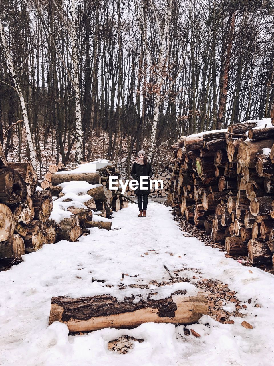 Woman standing amidst logs on snow covered field