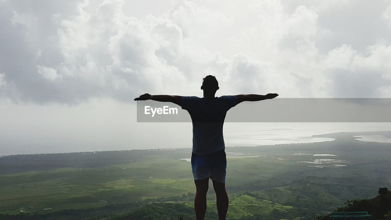 Rear view of man with arms outstretched standing against landscape and sky