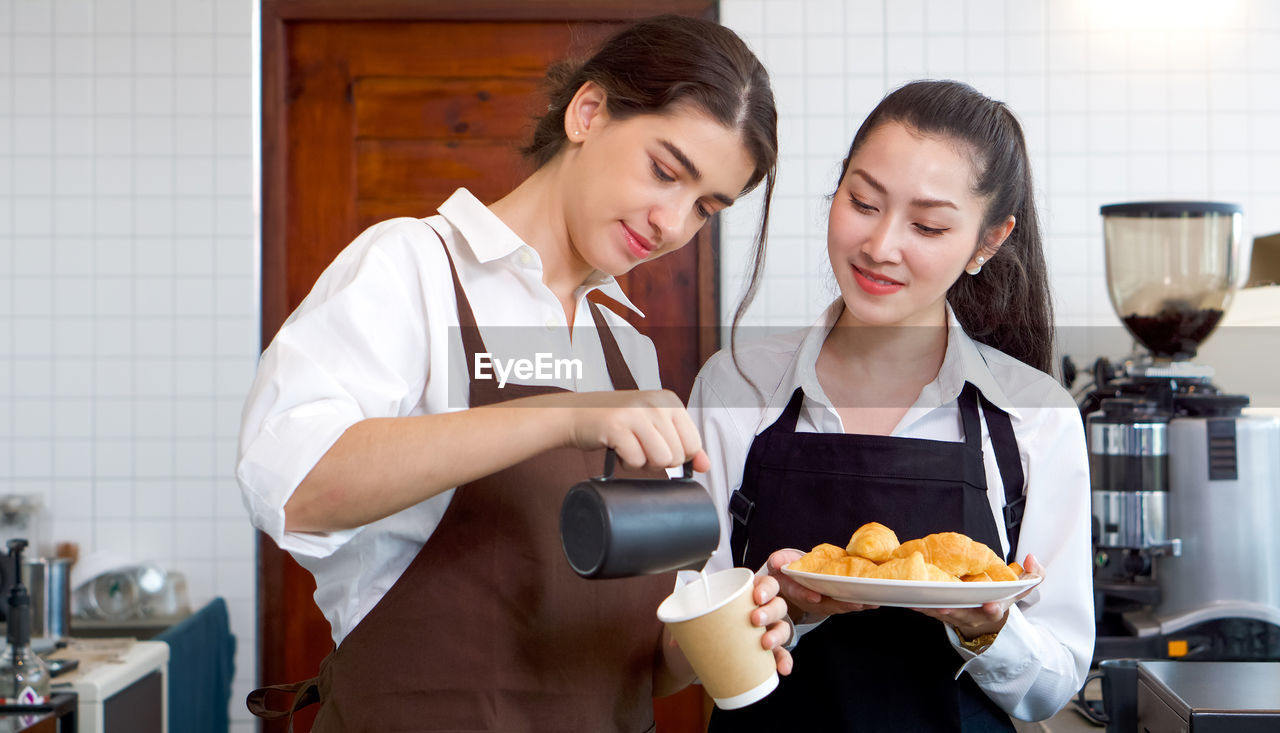 Young caucasian barista pouring milk from the jug into a paper coffee cup. 