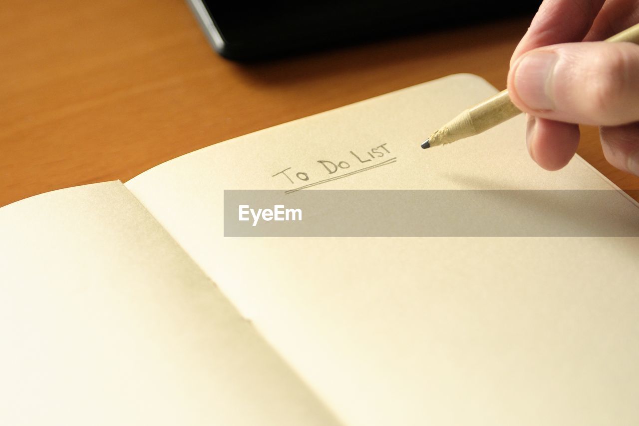 Cropped hand of man writing in notepad at desk in office