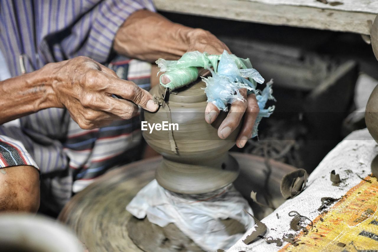 Midsection of man making earthenware on pottery wheel
