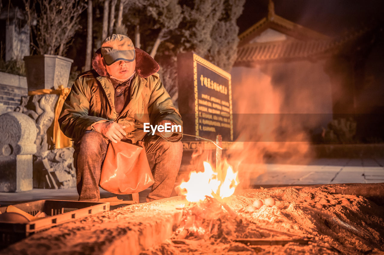 Man sitting by bonfire at night