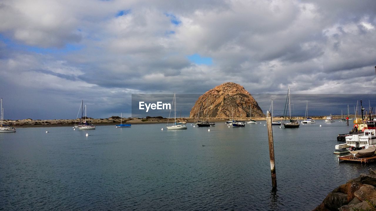 Boats moored in sea by rock against sky