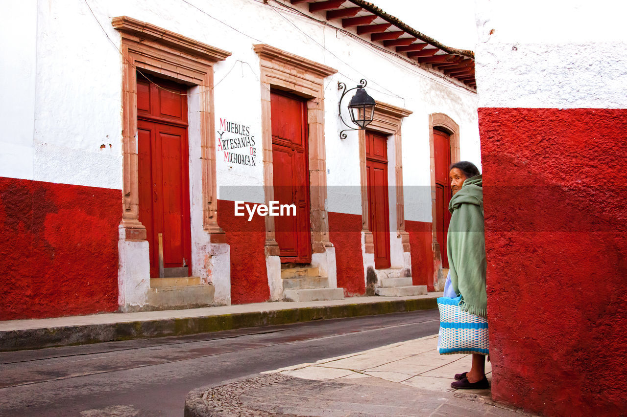 REAR VIEW OF WOMAN STANDING BY RED BUILDING