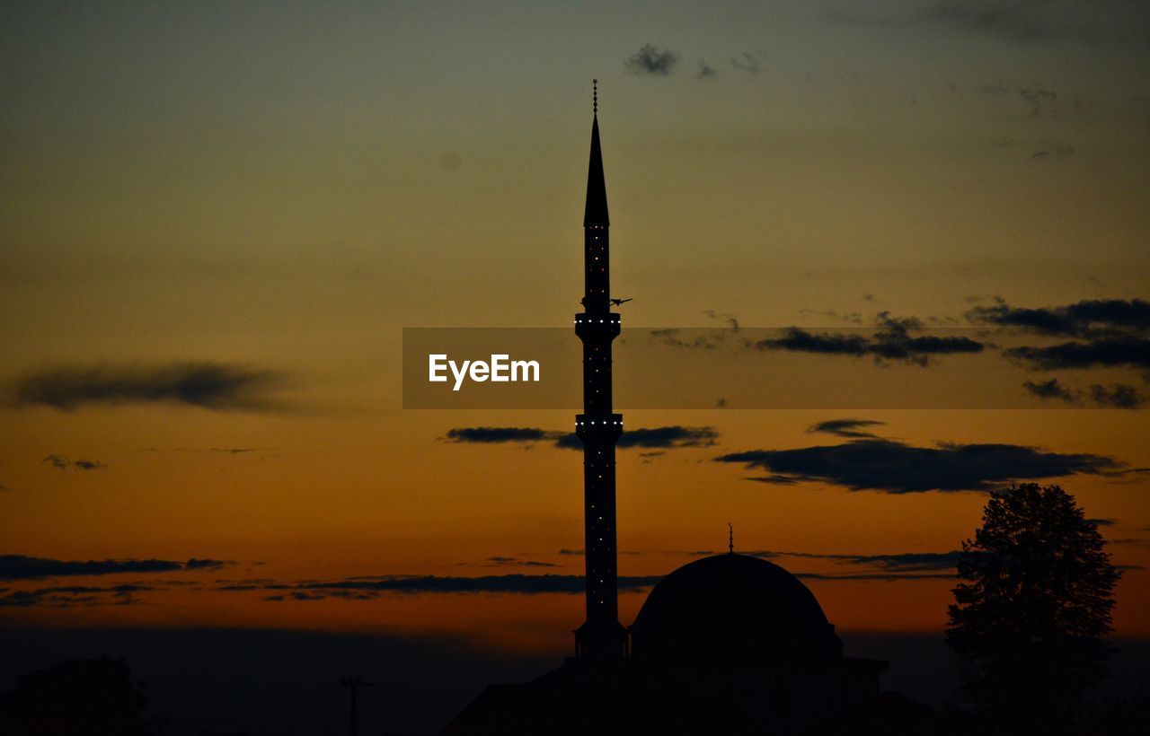 Silhouette tower by building against sky during sunset