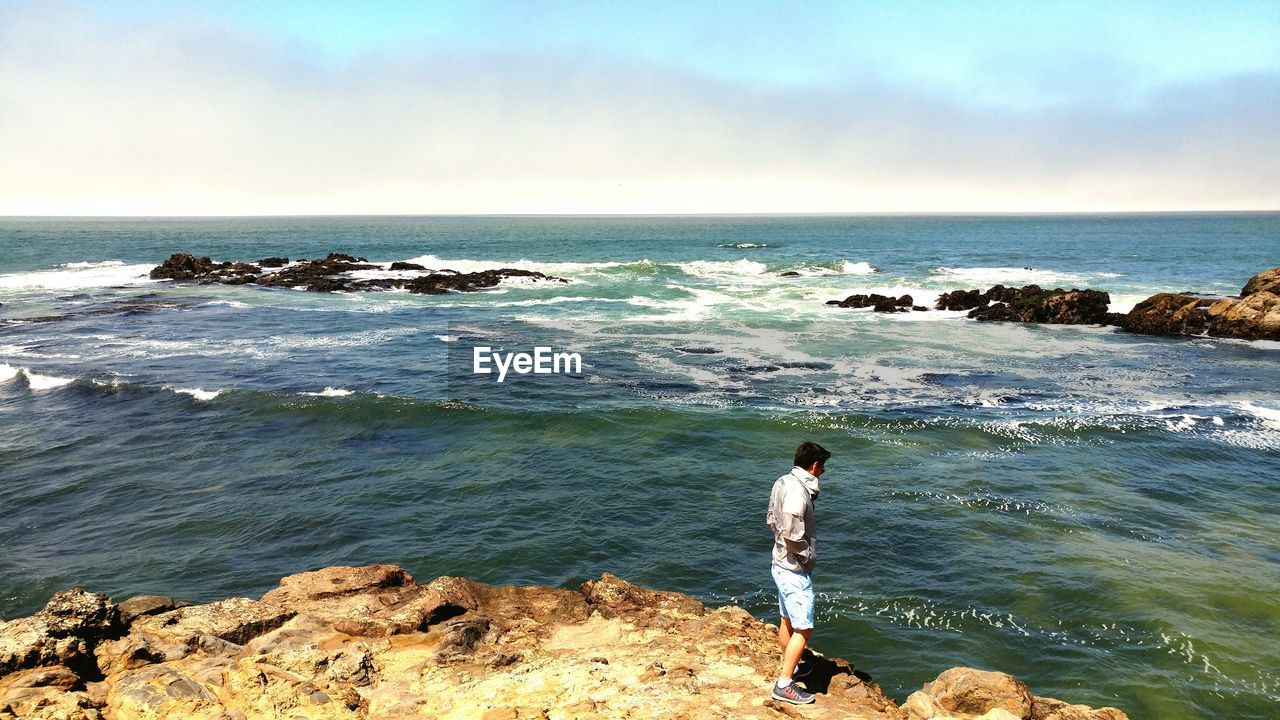 Man standing at sea shore against sky