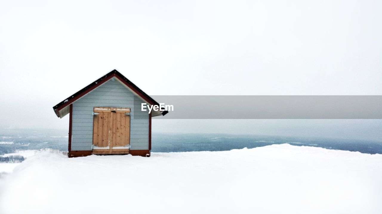 SNOW COVERED HOUSE BY BUILDING AGAINST SKY