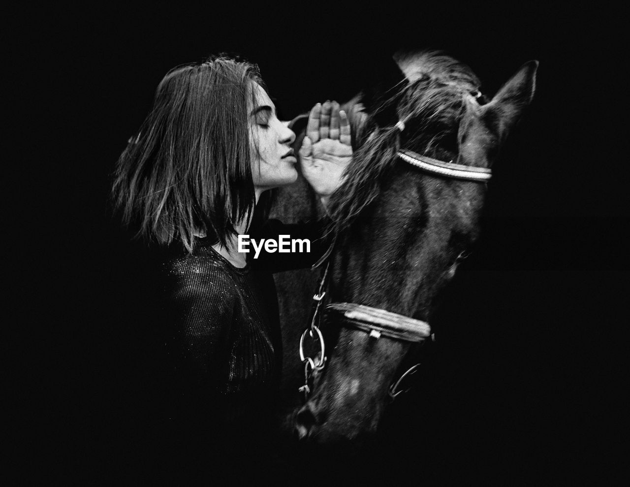 Woman standing with horse against black background