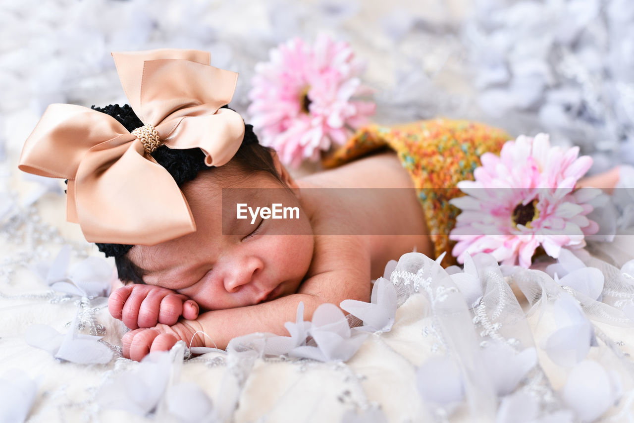 Close-up of cute baby girl with flowers sleeping on bed