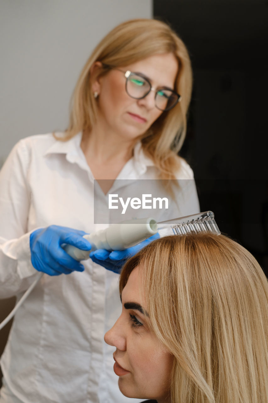 Doctor examines head skin of a young girl with special dermatology equipment system, hair loss and