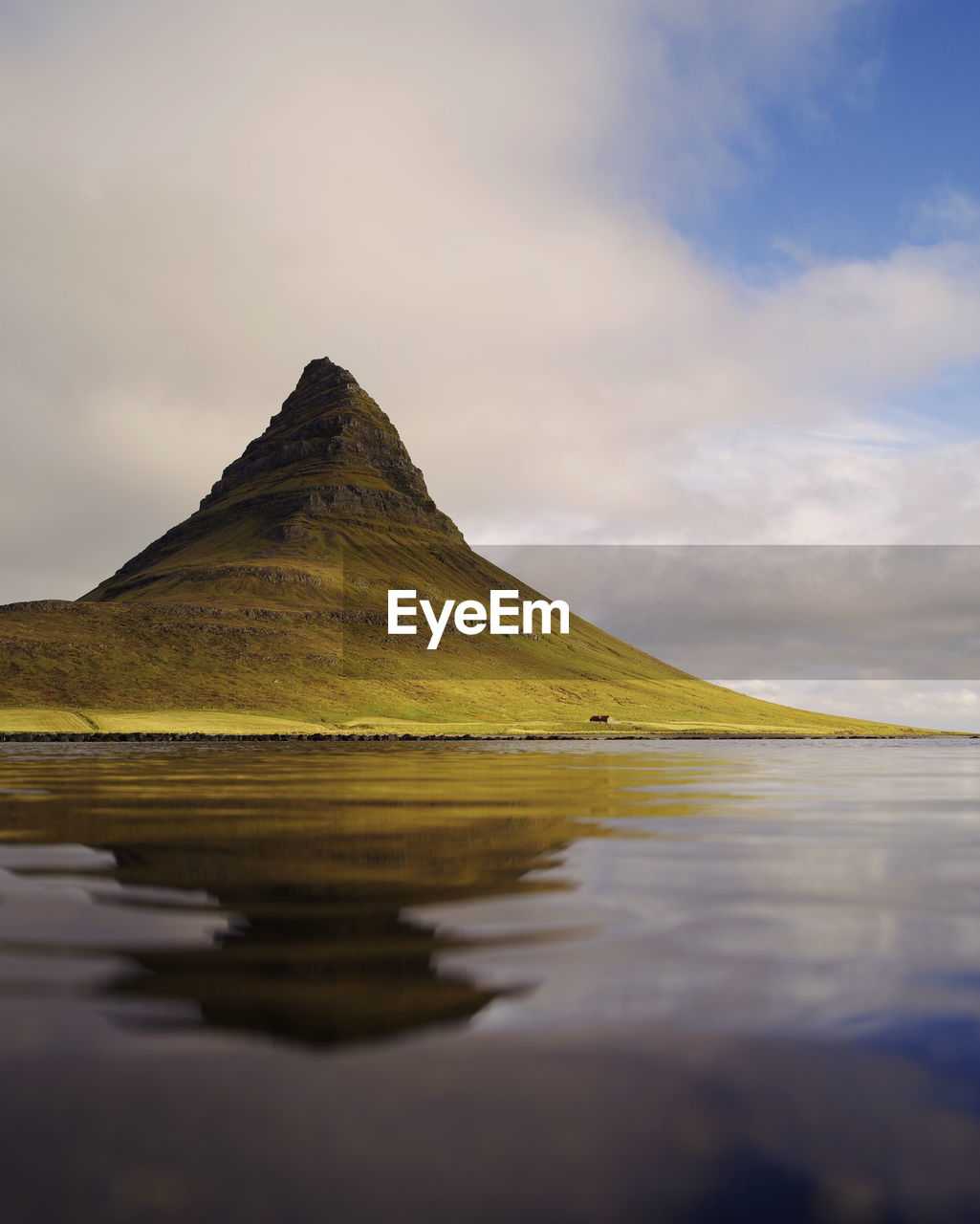 Scenic view of sea by mountain against cloudy sky