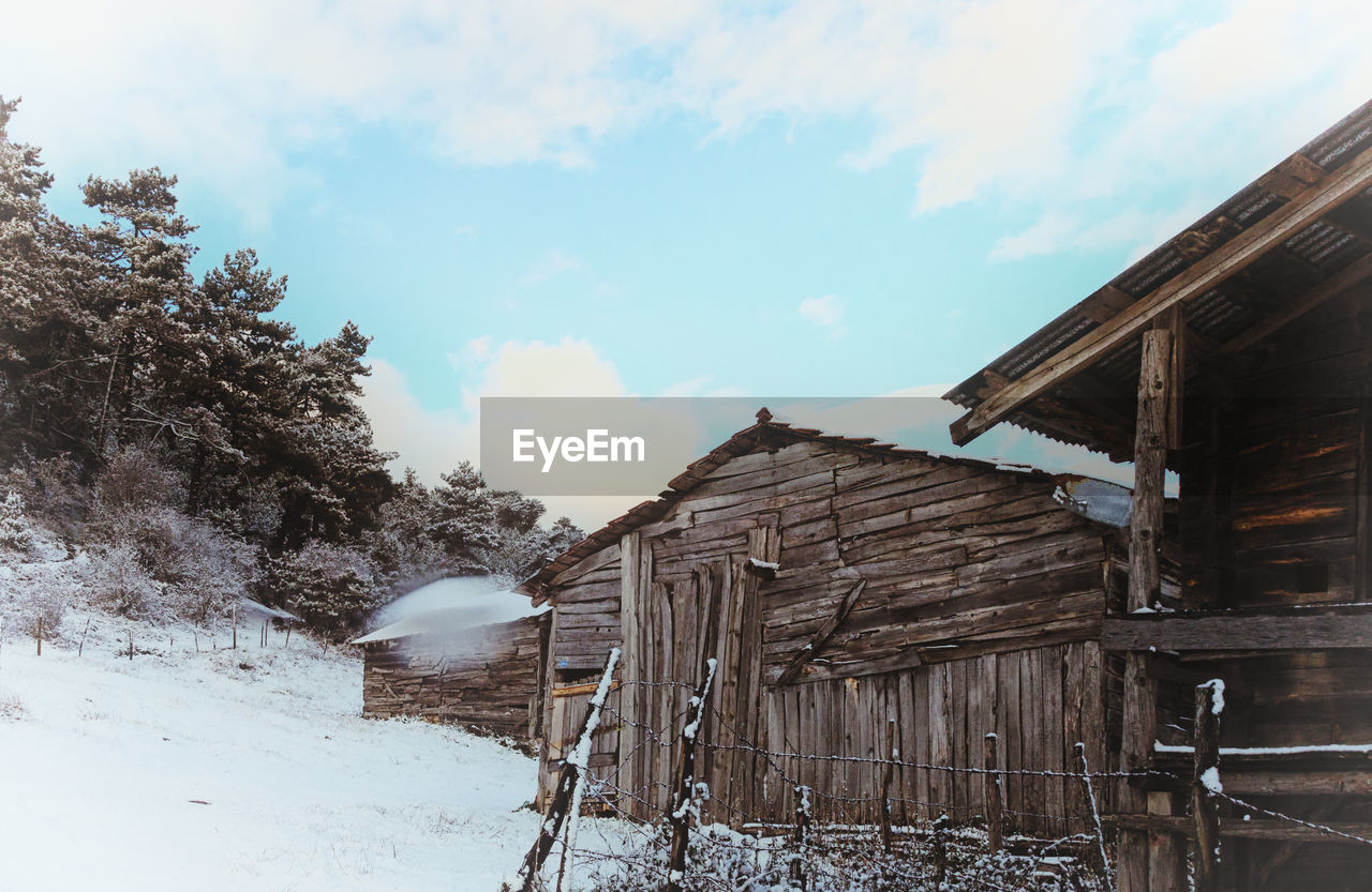 Wooden structure on snow covered field against sky