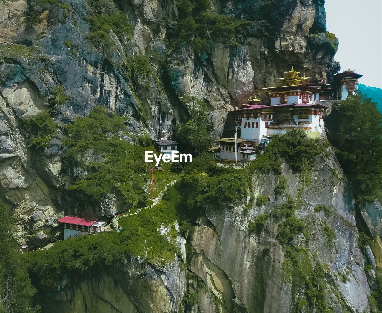 TREES AND ROCKS BY BUILDINGS AGAINST MOUNTAIN