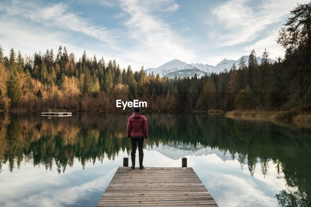 Rear view of human standing on pier over alpine lake against sky