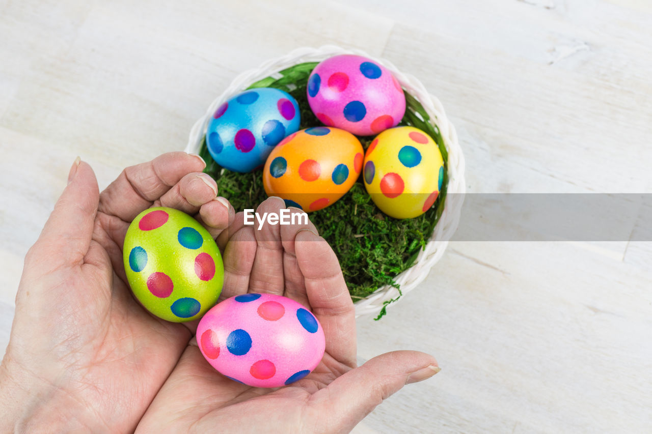 Cropped hands holding colorful easter eggs on table