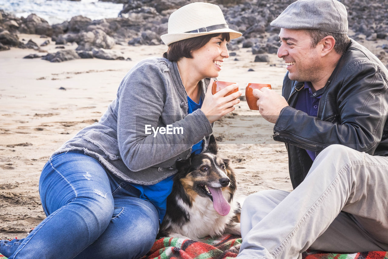 Couple having tea with dog on shore at beach