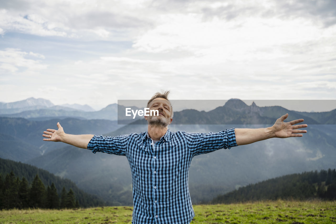 Carefree man standing with arms outstretched on mountain during vacation