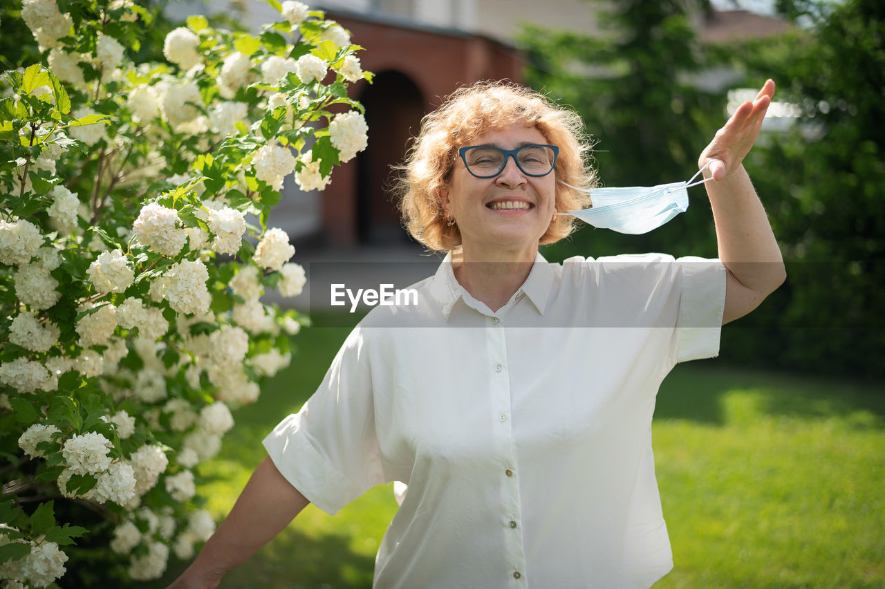 Smiling young woman standing by white flowering plants