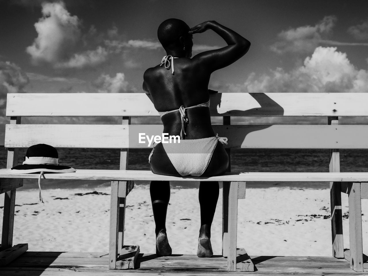 Rear view of woman sitting on bench at beach