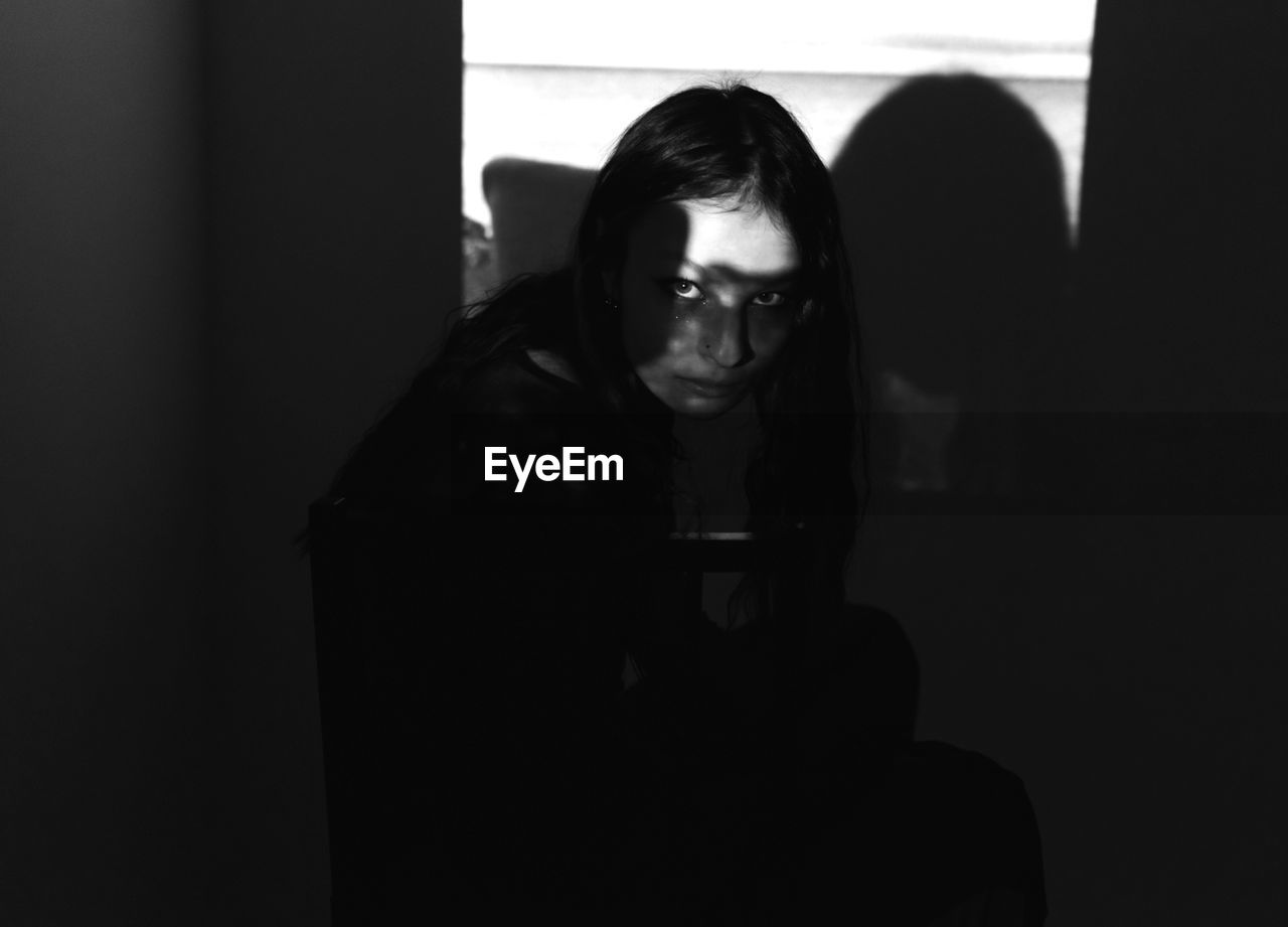 High angle portrait of young woman crouching in darkroom at home