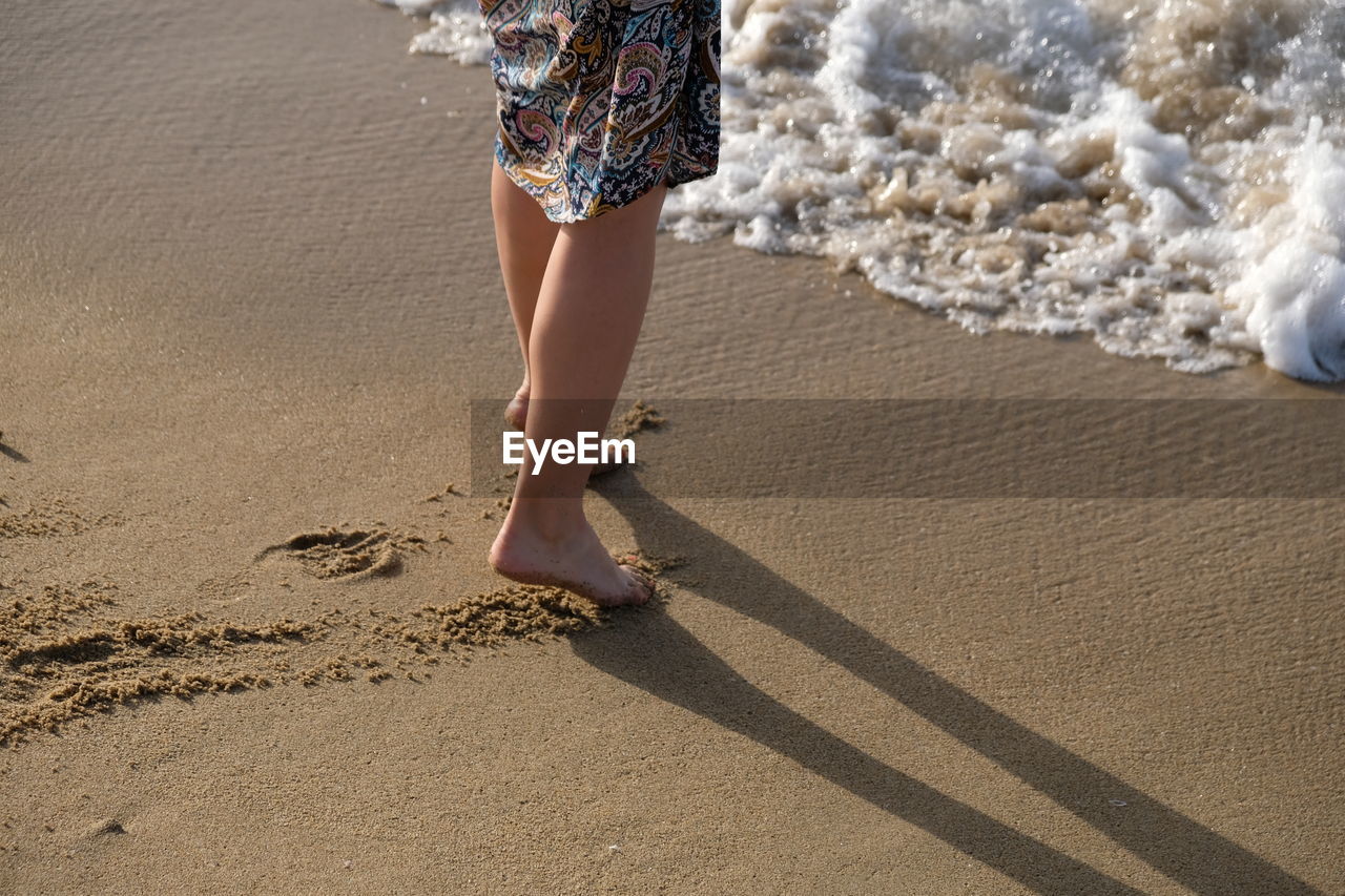 Low section of woman walking on shore at beach