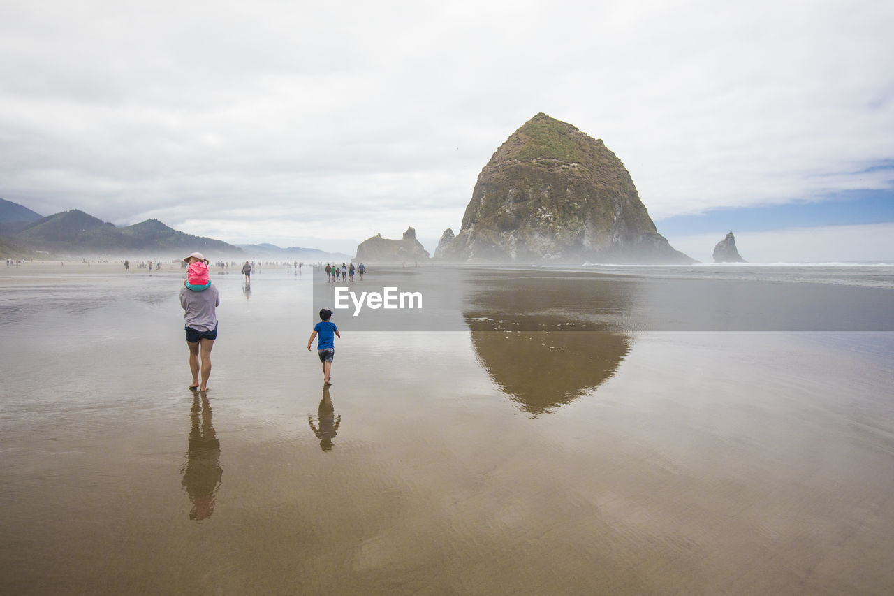 Rear view of mother and two kids walking on cannon beach.