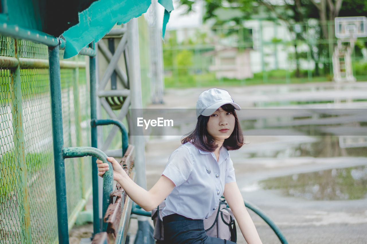 Portrait of young woman sitting on bench at basketball court