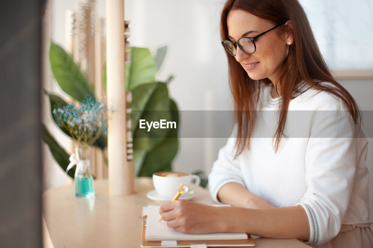 Smiling woman writing on diary while sitting at office