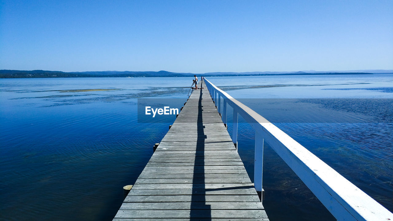 Wooden pier on sea against clear blue sky