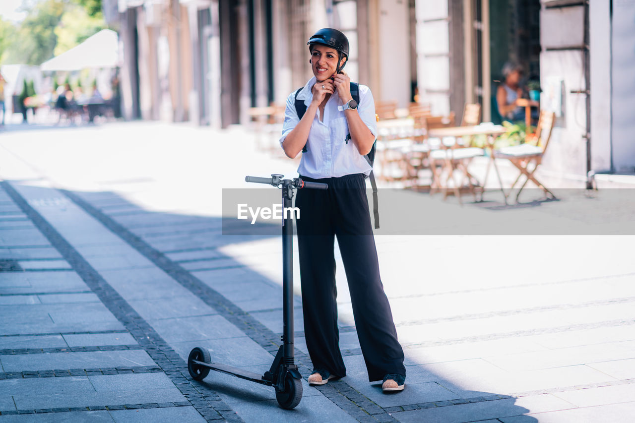Smiling woman wearing helmet while standing by electric push scooter on road