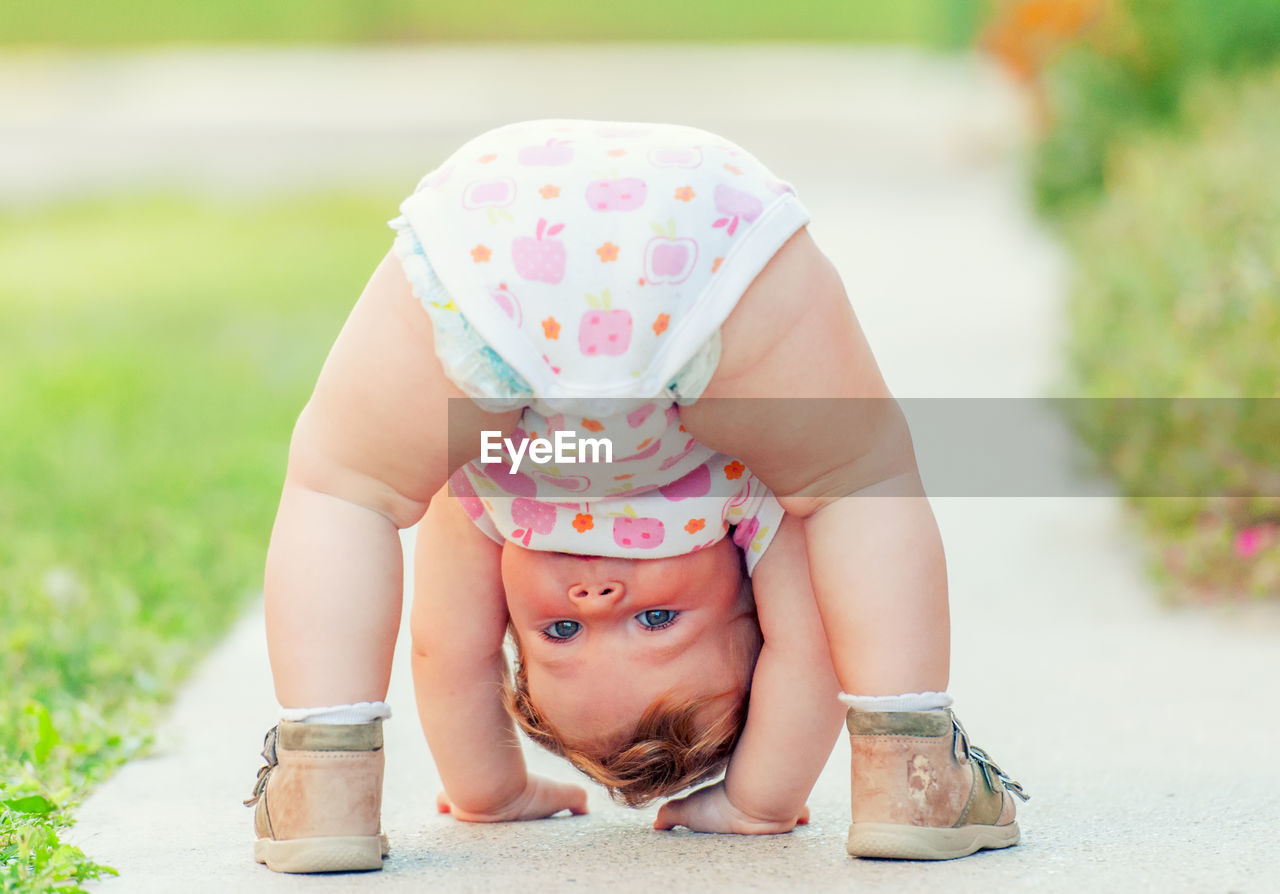 Portrait of cute baby girl with upside down standing on footpath