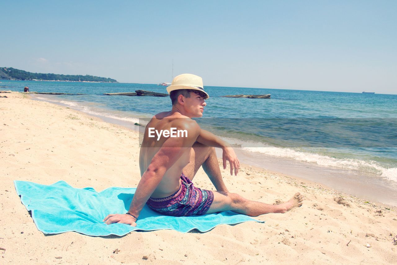 Shirtless man relaxing at beach against clear sky