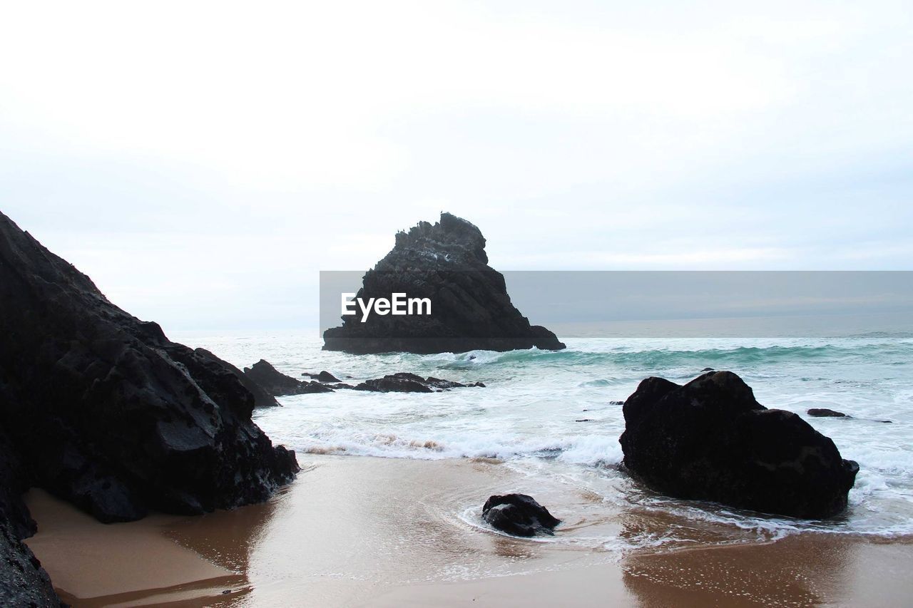 Rocks on cliff by sea against sky