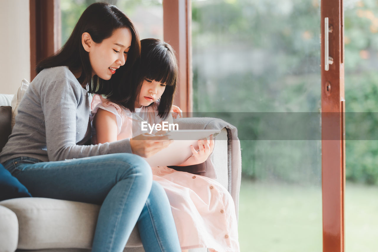 WOMAN USING PHONE WHILE SITTING ON WINDOW