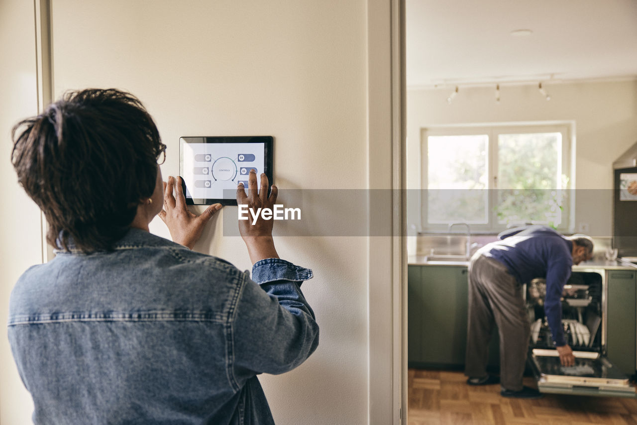 Senior woman wearing denim jacket using home automation on wall