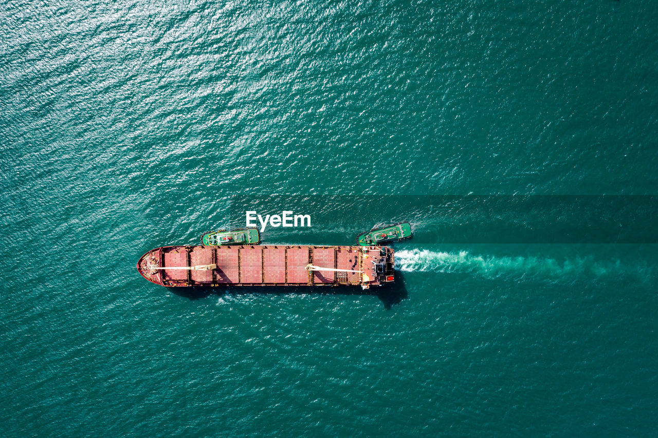 Aerial top view tugboat drag oil ship tanker on green sea going to shipyard repair and maintenance