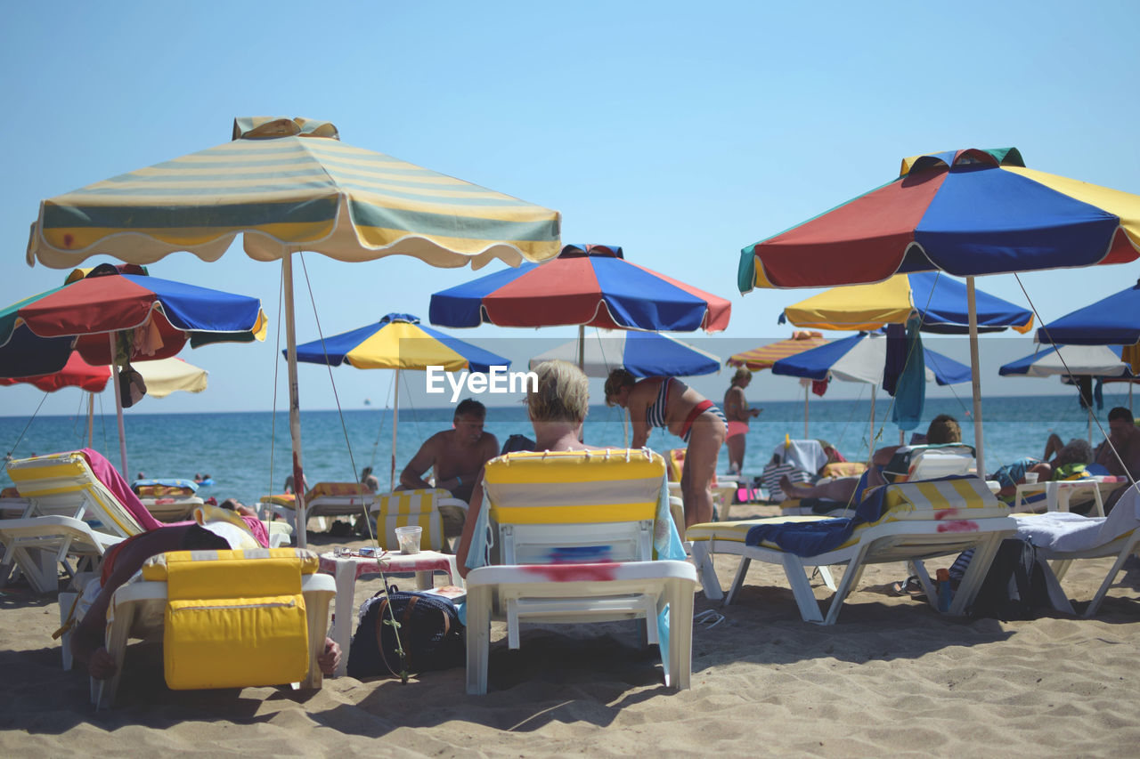 REAR VIEW OF PEOPLE RELAXING ON BEACH