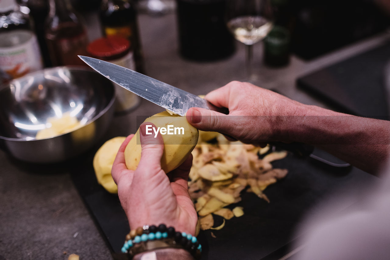 From above anonymous person with bracelet using sharp knife to peel fresh potato over in kitchen during cooking lesson in navarre, spain person