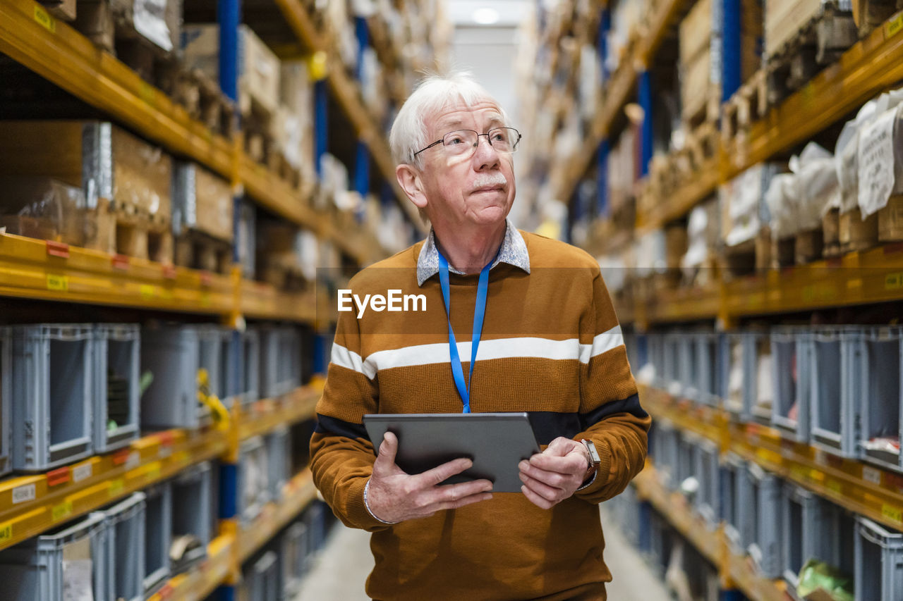 Senior man with tablet pc examining stock at warehouse