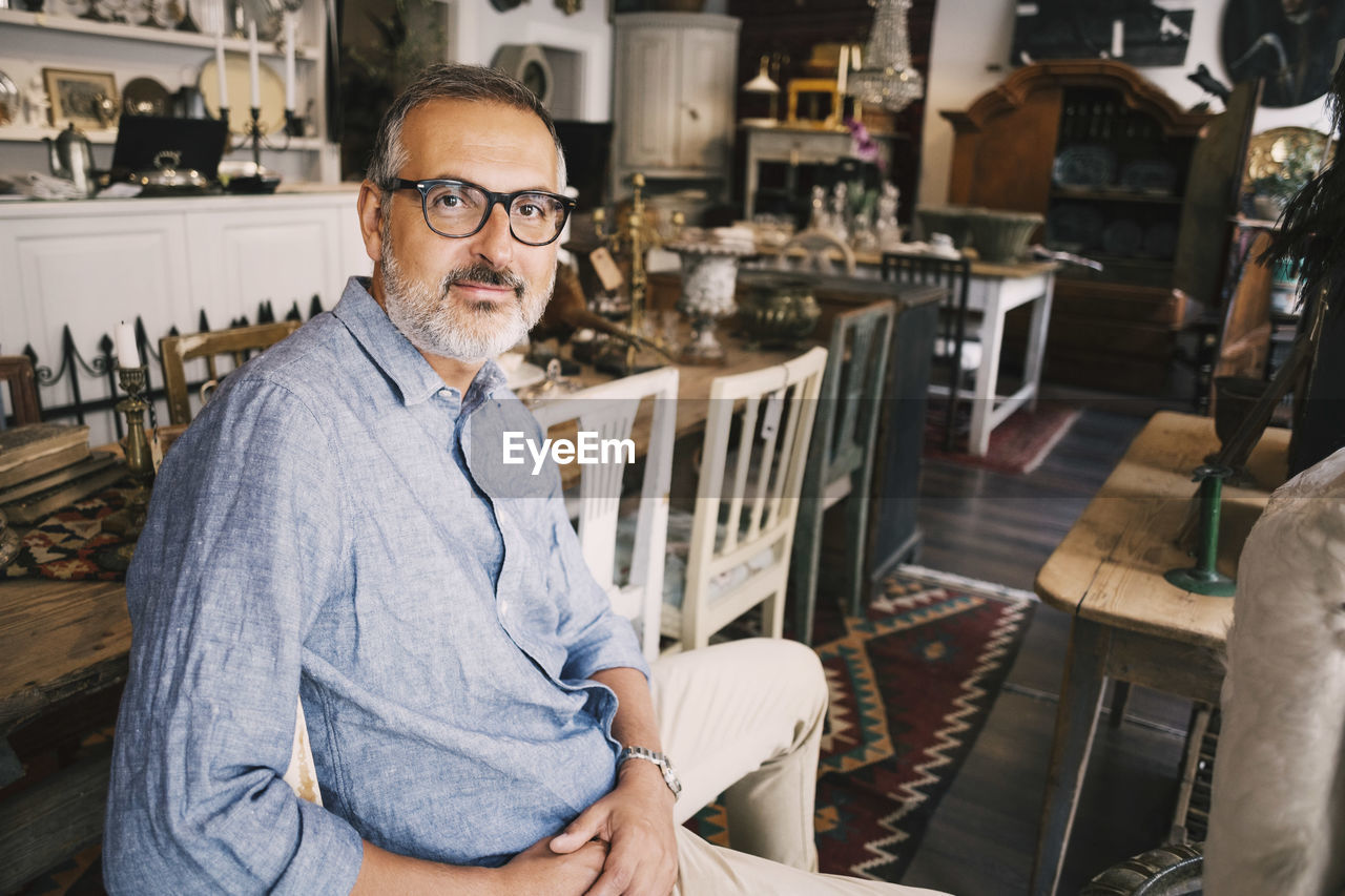 Portrait of confident owner sitting on chair at table in antique store