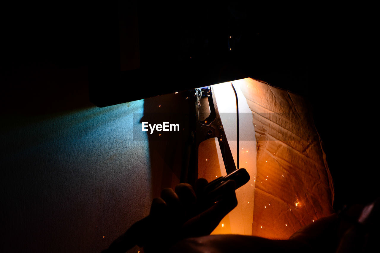 Cropped image of welder hand welding in darkroom