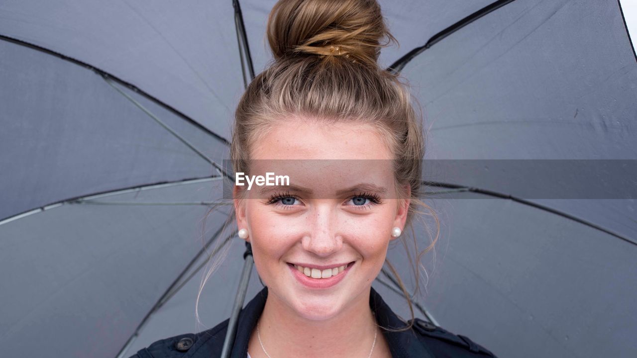 Portrait of smiling teenage girl carrying umbrella while standing outdoors