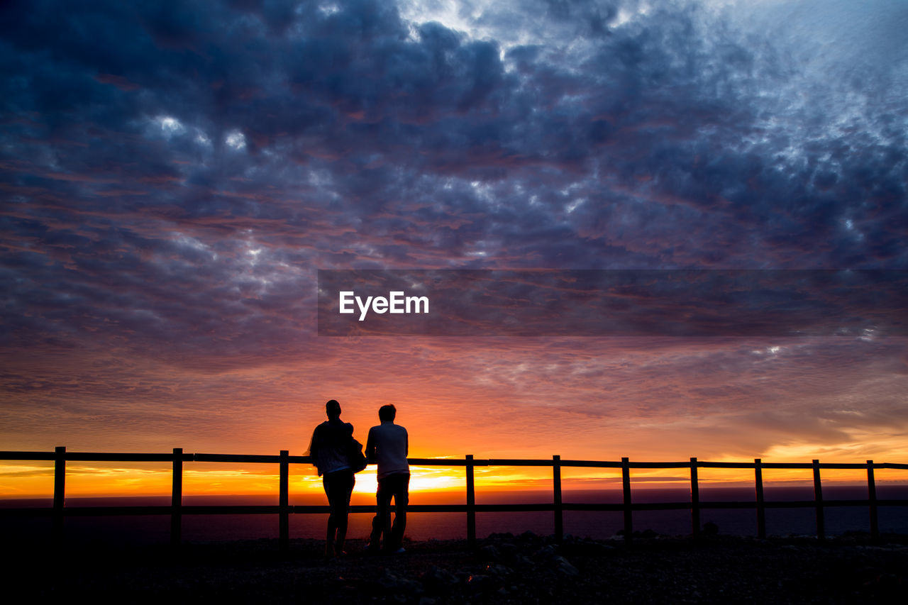 Couple standing against cloudy sky during sunset