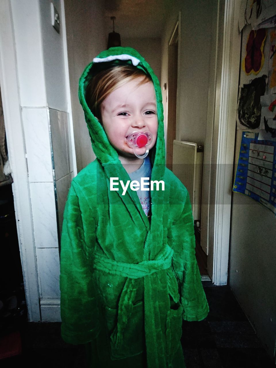 Boy with pacifier in mouth wearing green bathrobe at home