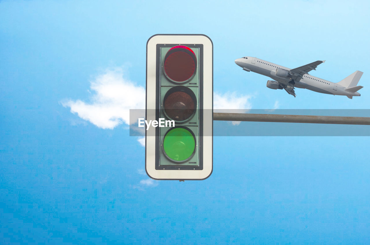 Low angle view of road signal and airplane against blue sky