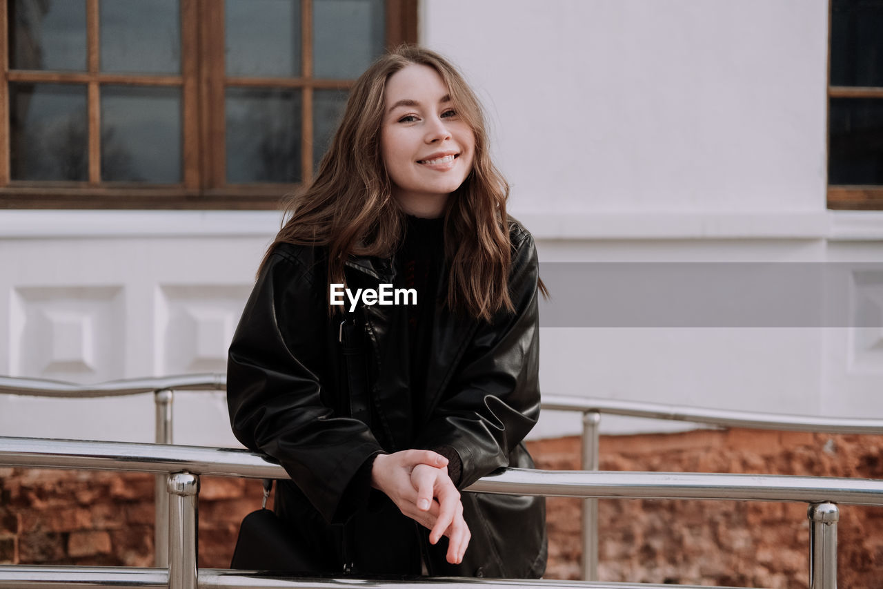 Portrait of smiling young woman standing against railing