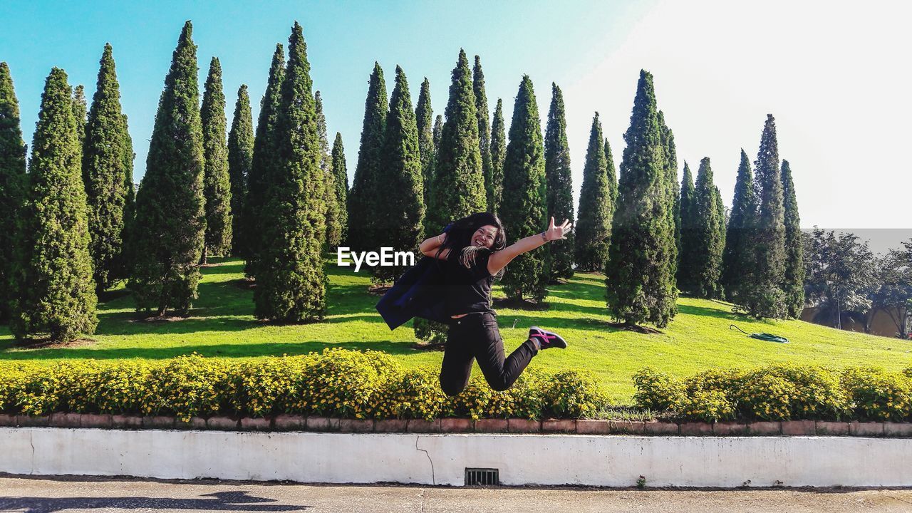 Front view of woman jumping against trees