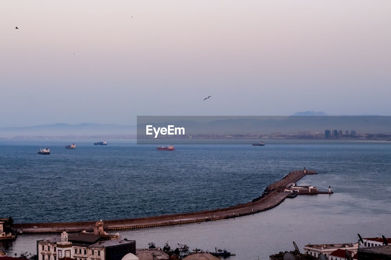 BIRDS FLYING OVER SEA AGAINST SKY
